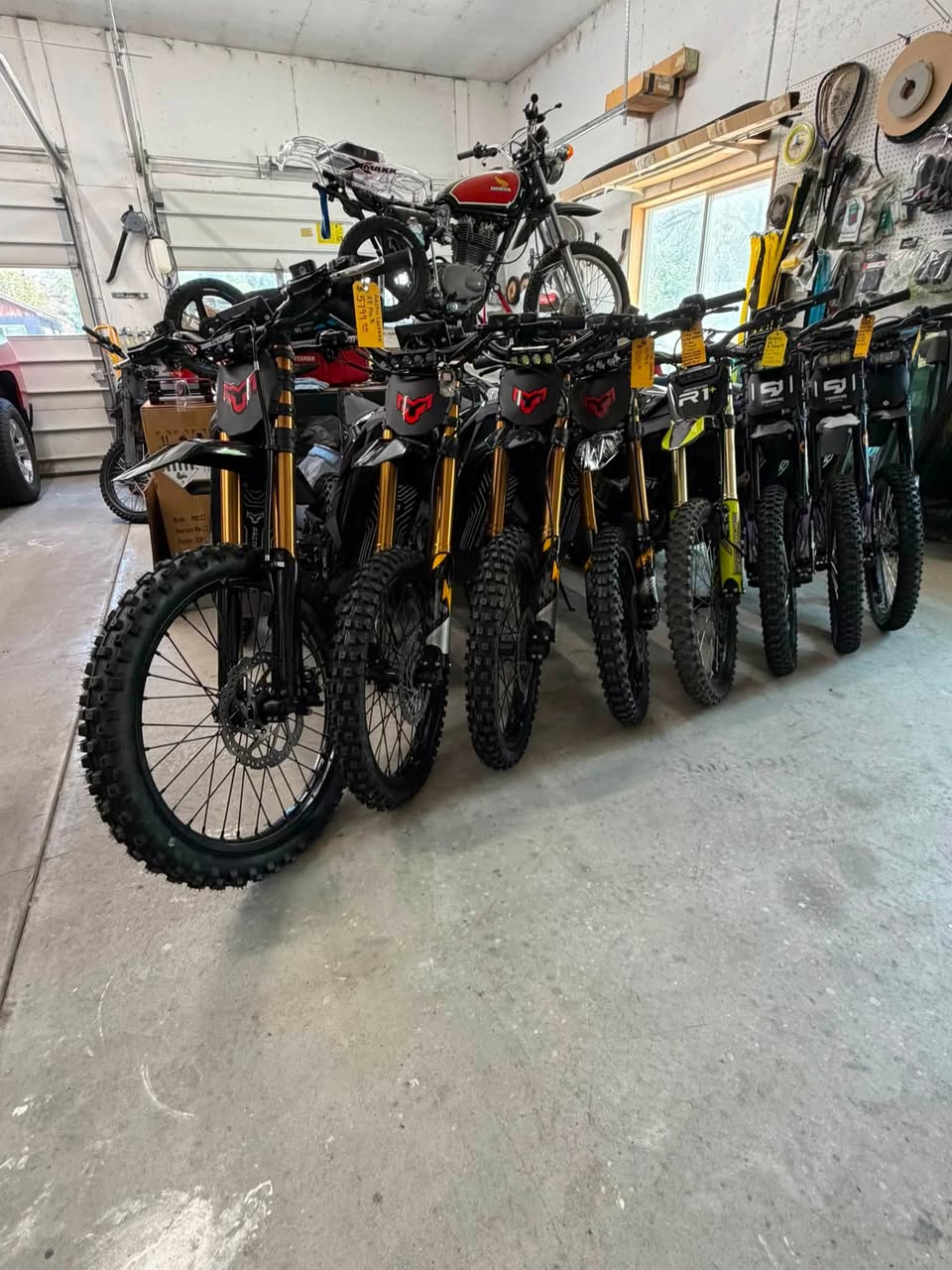 Electric dirt bikes lined up in the B&L Specialties garage bay next to a vintage Honda motorcycle.